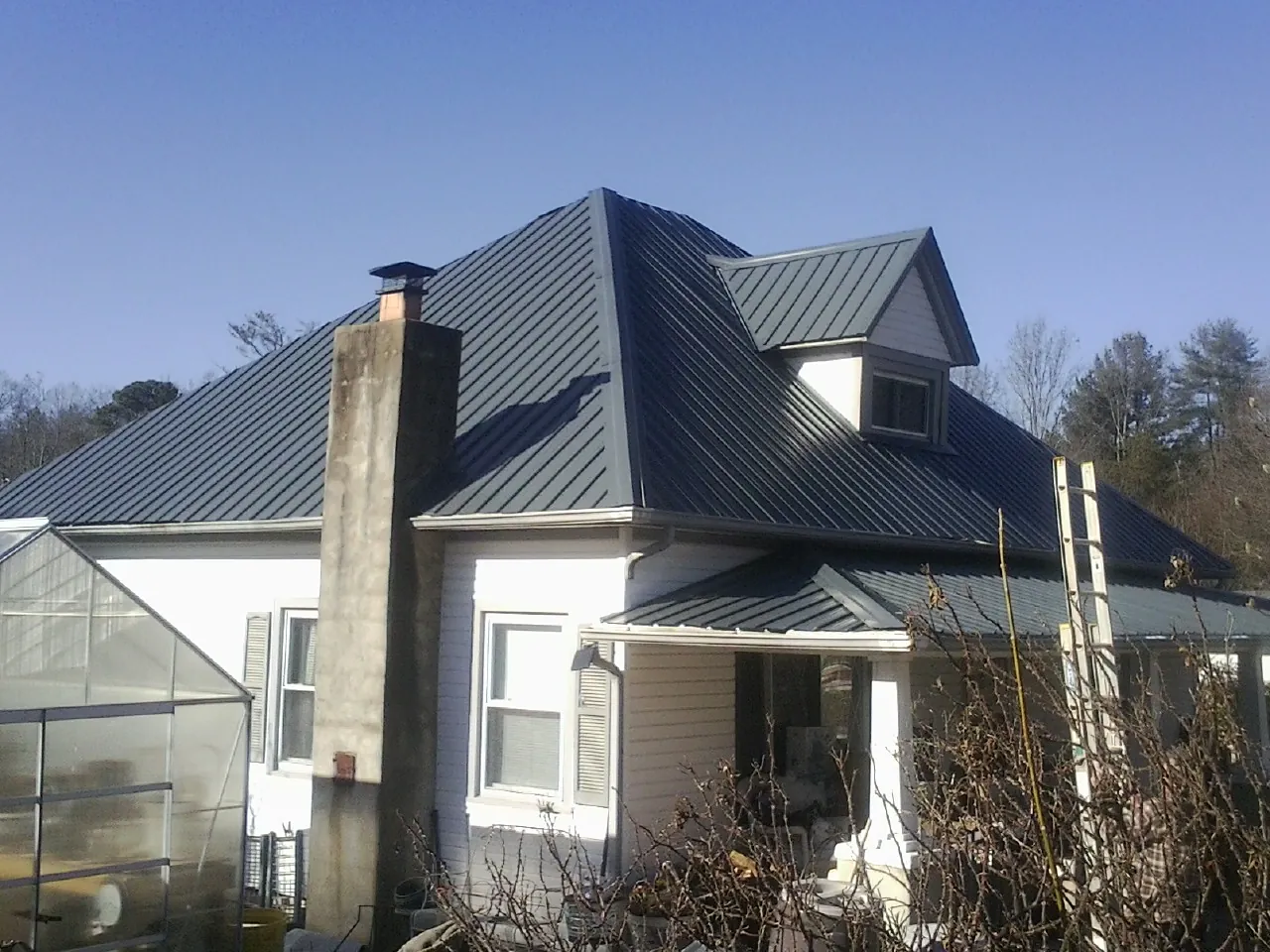 Dark blue standing seam metal roof on a white farmhouse with dormer — Slate & Tile Roof Repair by Roofing Brothers in Twin City