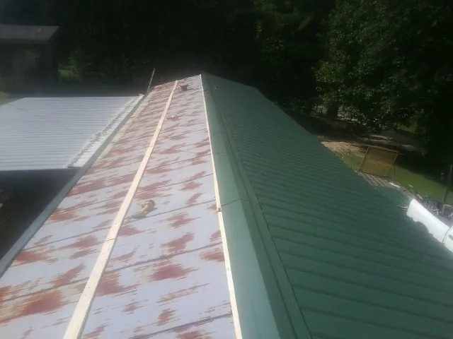 Old rusted panels beside newly installed green metal roofing — Wind Damage Roof Repair by Roofing Brothers in Twin City
