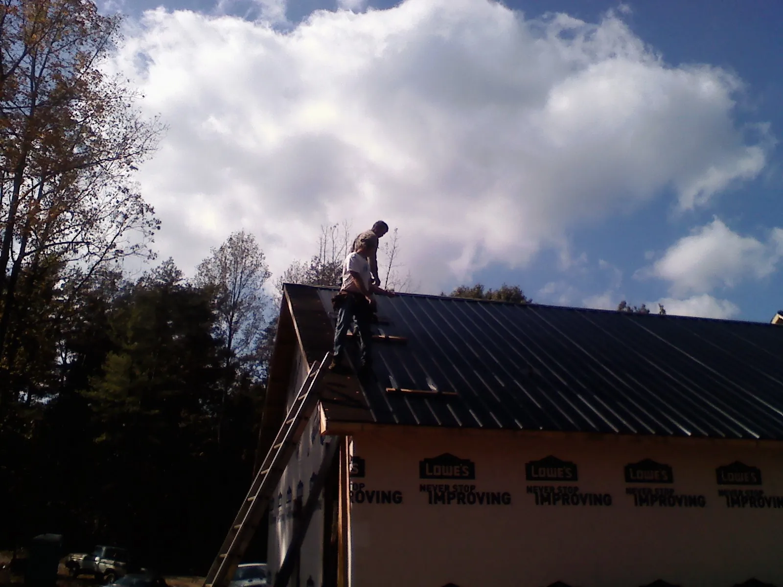 Roofer fastening dark metal panels high against a cloudy sky, from a Roof Inspection job in Twin City