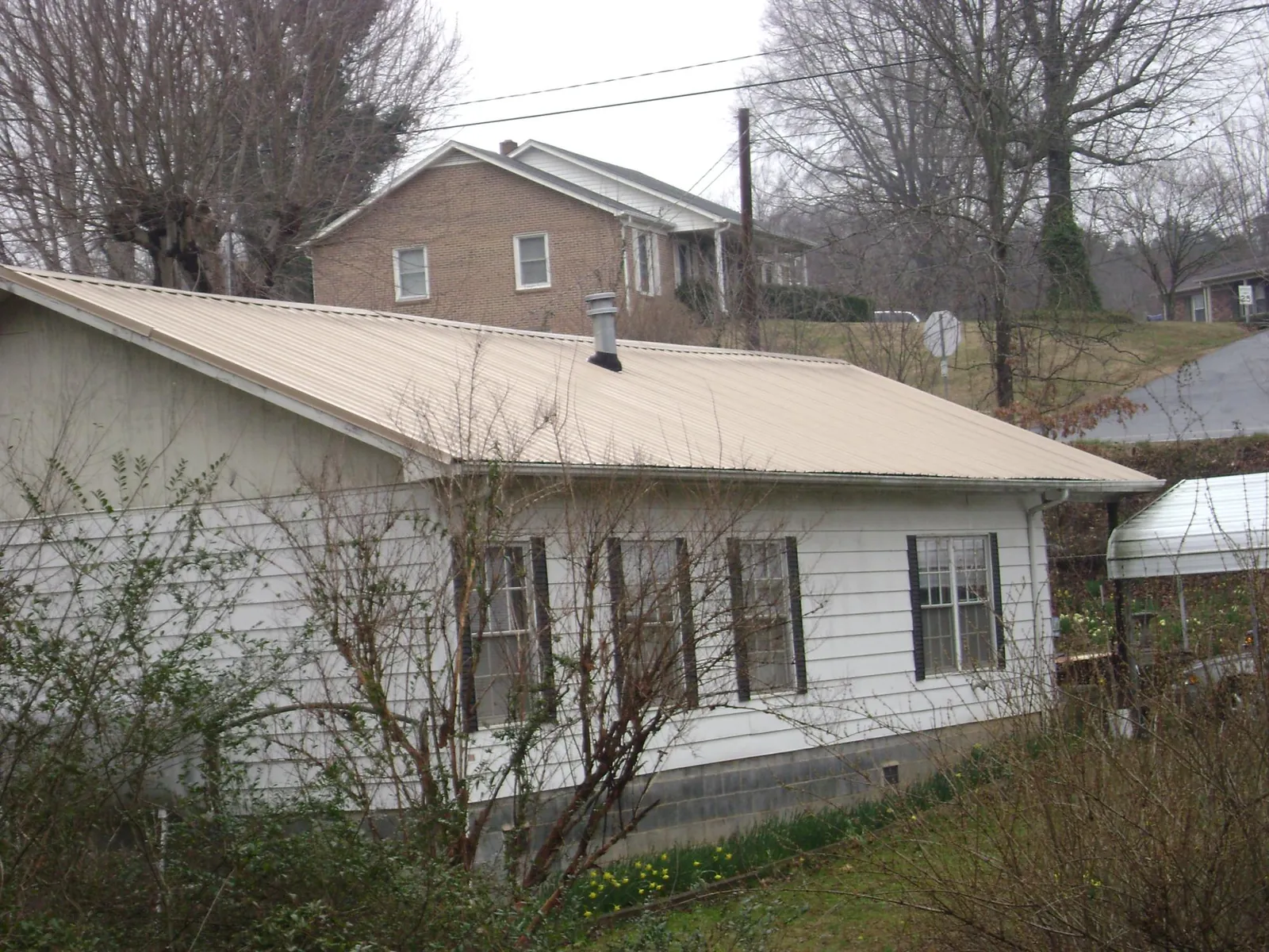 Tan metal roof on a white sided house set into a hillside — Commercial Roofing by Roofing Brothers in Twin City